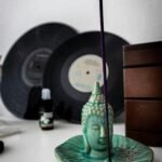 A Buddha-shaped incense holder beside vinyl records on a table.